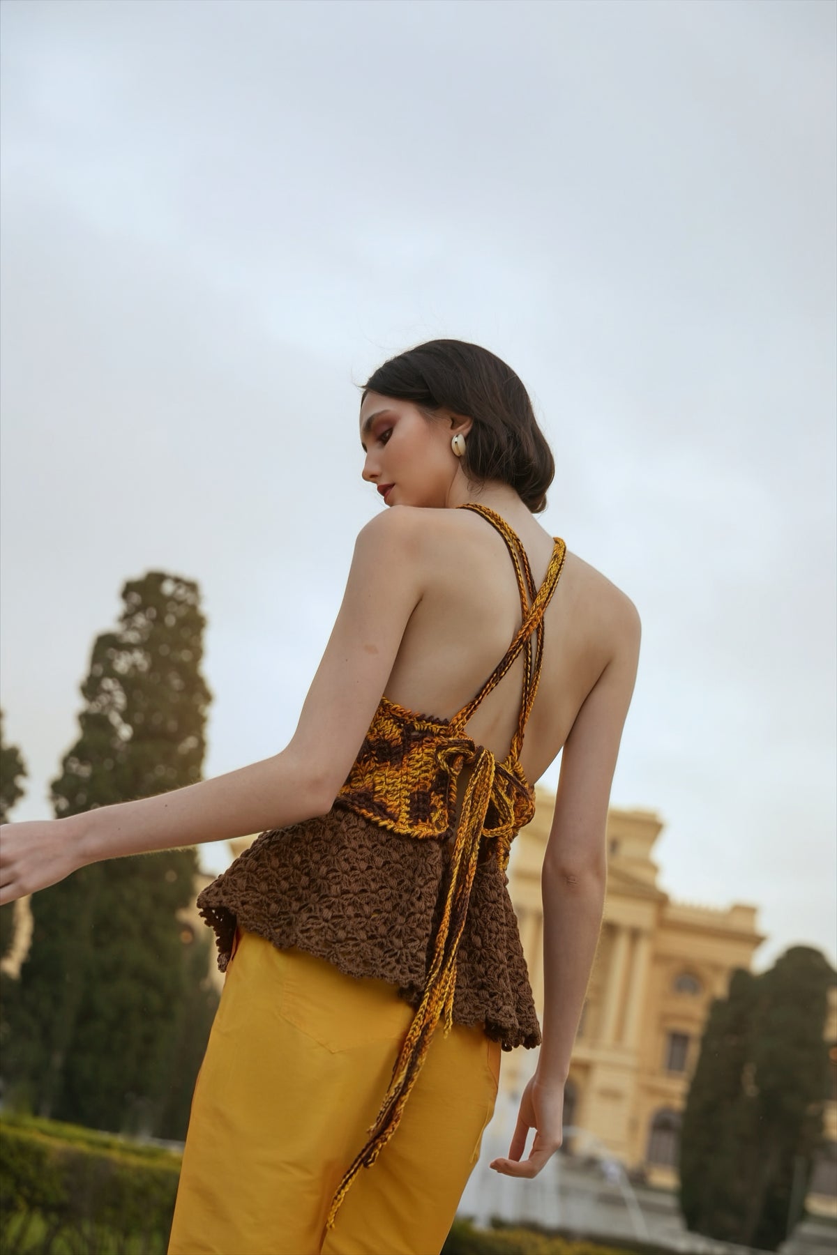 Blusa frente única feita à mão, em tons de amarelo, laranja e marrom, com peplum de renda marrom. Calça tafetá amarela. Tudo da marca Isabela Monteiro.