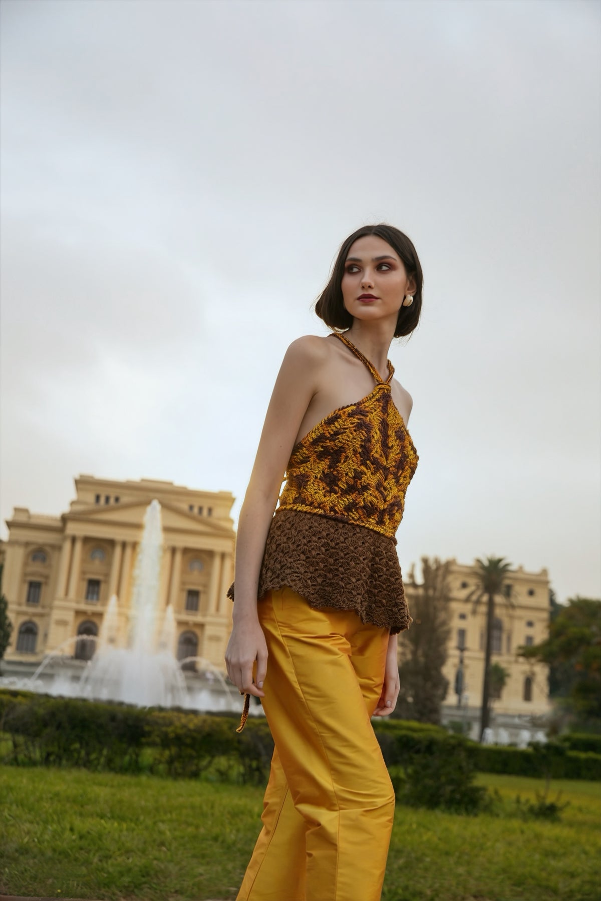 Blusa frente única feita à mão, em tons de amarelo, laranja e marrom, com peplum de renda marrom. Calça tafetá amarela. Tudo da marca Isabela Monteiro. 
