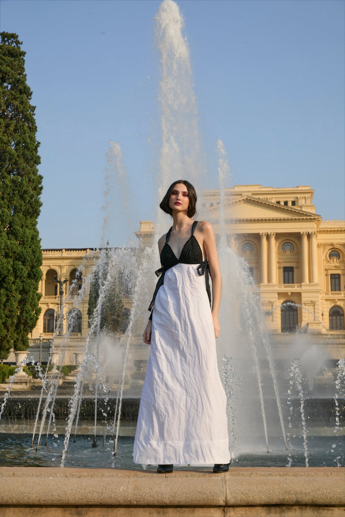 Vestido longo preto e branco da marca Isabela Monteiro. Decote realçado pelo bojo preto feito à mão em crochê. Costas nuas com decote de fitas cruzadas em laço nas laterais. Saia longa branca em algodão e inox para efeito amassado descontraído. Bolsos nas costuras laterais. 